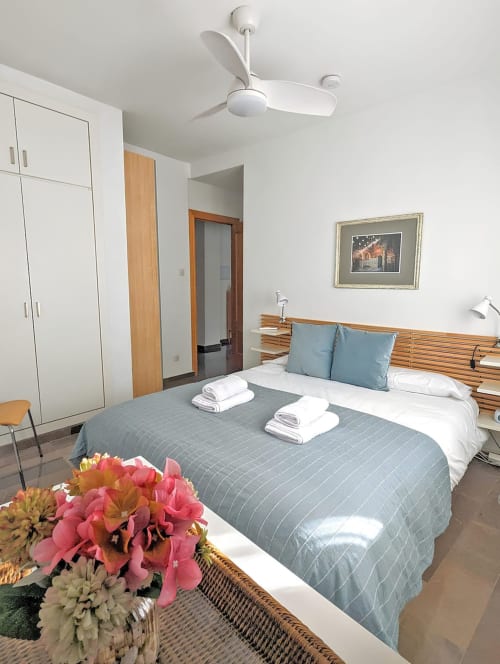 Dormitorio con cama doble, ropa de cama azul, ventilador de techo y decoración floral en apartamento turístico.