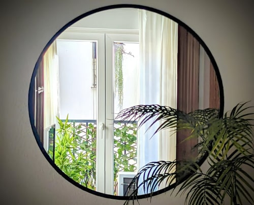 Reflejo de una ventana con plantas decorativas y cortinas blancas visto a través de un espejo redondo