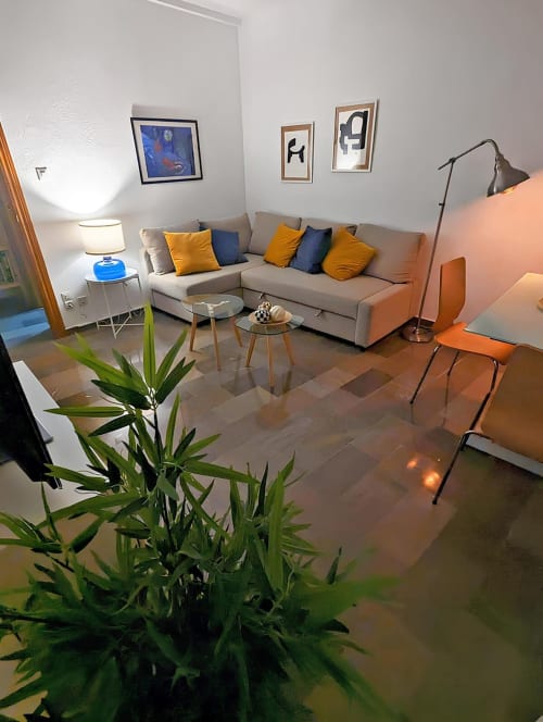 Sala de estar iluminada con sofá en tonos beige, cojines azules y amarillos, bambú decorativo y mesas de cristal modernas.