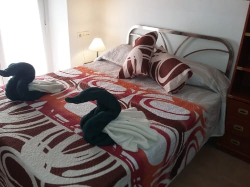 Dormitorio con cama doble, colcha colorida y toallas en forma de cisne, ideal para una estancia acogedora y especial.