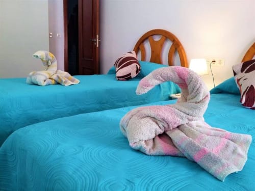 Habitación con camas turquesa, toallas en forma de cisne y detalles decorativos que crean un ambiente acogedor.