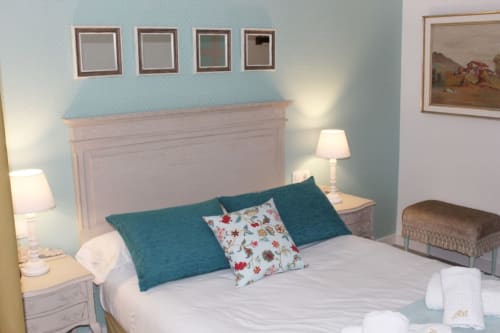Dormitorio acogedor con paredes en azul suave, lámparas elegantes y cojines coloridos que añaden un toque fresco.