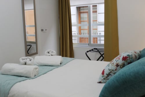 Habitación de hotel con cama doble, ropa de cama blanca, toallas limpias y ventana luminosa con cortinas.
