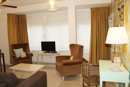 Salón moderno con sofá marrón, sillones a juego, mesa de centro y TV. Cortinas doradas y pared decorativa.