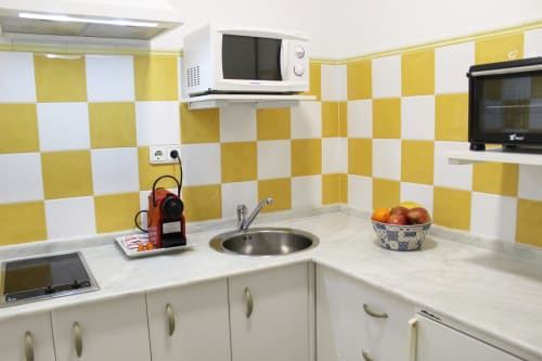 Cocina moderna con detalles coloridos en los azulejos, microondas y una cesta con frutas frescas sobre la encimera.