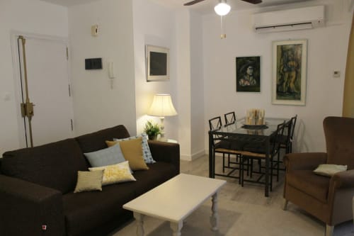 Salón moderno con sofá marrón, sillón, mesa de centro, comedor en apartamento de Granada. Decoración con cuadros.