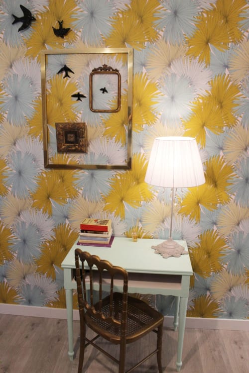 Escritorio vintage verde con libros, lámpara y silla de madera. Pared con papel pintado floral y cuadros en apartamento de Granada.
