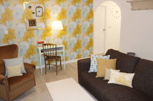 Salón moderno con sofá marrón, sillón a juego, pared de flores y mesa de centro blanca. Decoración con cuadros y lámpara.