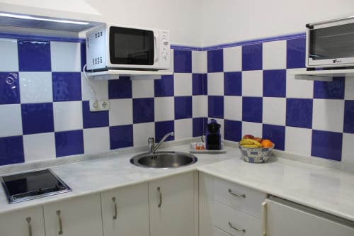 Cocina moderna con azulejos azules y blancos, microondas, horno, vitrocerámica y nevera. Diseño funcional y luminoso.