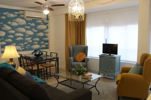 Salón moderno con sofá, mesa, TV y sillones. Pared con papel de nubes, cortinas doradas y diseño acogedor y luminoso.