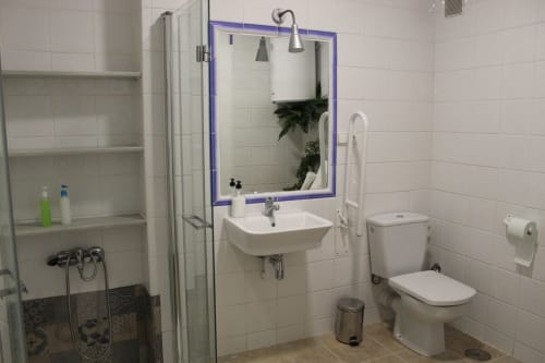Baño moderno con ducha, lavamanos, inodoro y espejo. Azulejos blancos, detalles morados y diseño funcional en un apartamento en Granada.