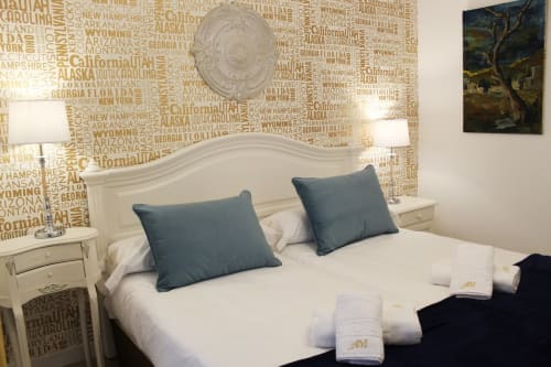 Dormitorio moderno con cama doble, ropa de cama blanca, cabecero de madera y pared con nombres de ciudades.