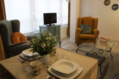Salón moderno con comedor, sillones, TV y mesa de cristal. Flores, cortinas y ambiente acogedor en un apartamento en Granada.