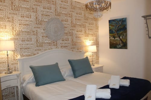 Dormitorio moderno con cama doble, cabecero blanco, ropa azul y blanca, pared con ciudades, lámparas a juego y toallas limpias.