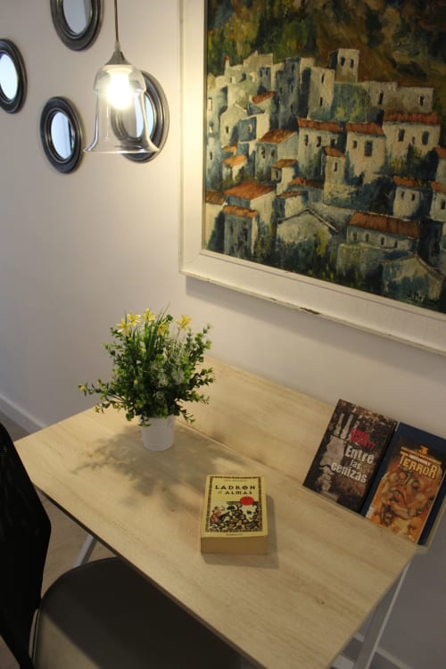 Mesa auxiliar con libros, planta y lámpara en salón con cuadro de paisaje urbano, ambiente acogedor y moderno en un apartamento en Granada.
