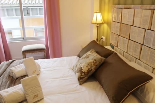 Habitación luminosa con cabecero de libros, cama elegante, cojines florales y cortinas rosas con detalles clásicos.