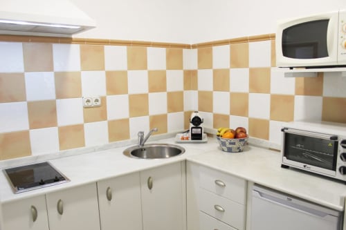 Cocina compacta con azulejos beige y blancos, electrodomésticos modernos y encimeras funcionales y luminosas.