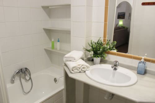 Baño con azulejos blancos, lavabo con decoración floral, bañera con grifo clásico y toallas impecables.