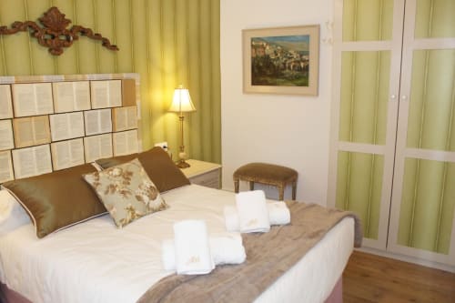 Habitación con cabecero de libros, armario verde, lámpara cálida, decoración clásica y detalles elegantes.