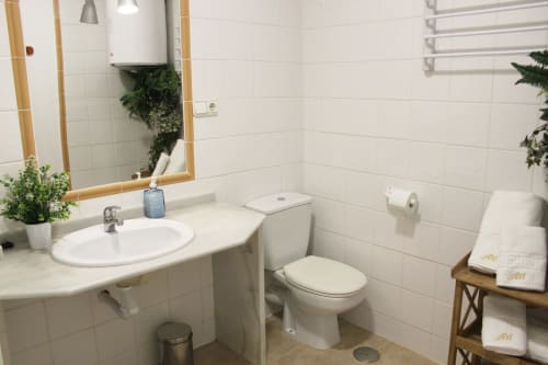 Baño luminoso con azulejos blancos, espejo con marco de madera, detalles verdes y toallas decorativas elegantes.