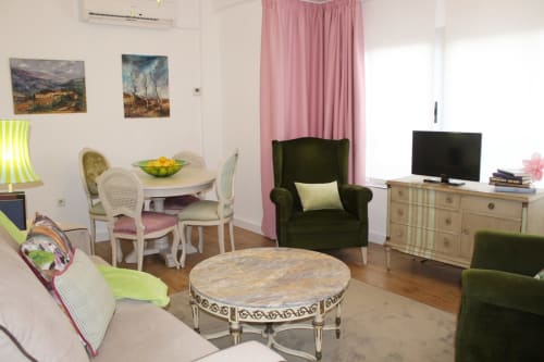 Salón elegante con sillones verdes, cortinas rosas, mesa de comedor clásica y detalles vintage en tonos suaves.