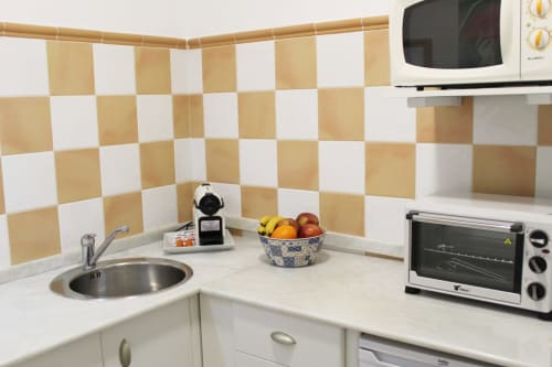 Cocina compacta con azulejos a cuadros beige y blancos, electrodomésticos modernos y detalles decorativos.