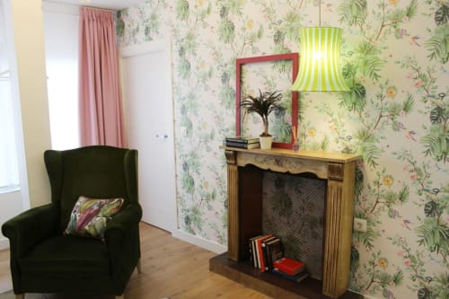 Rincón decorativo con sillón verde, chimenea vintage, papel floral y lámpara colgante con detalles vibrantes.