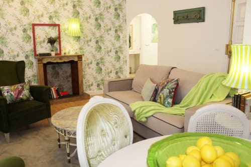 Salón vibrante con sofá beige, sillón verde, chimenea decorativa, papel floral y mesa con centro de limones.