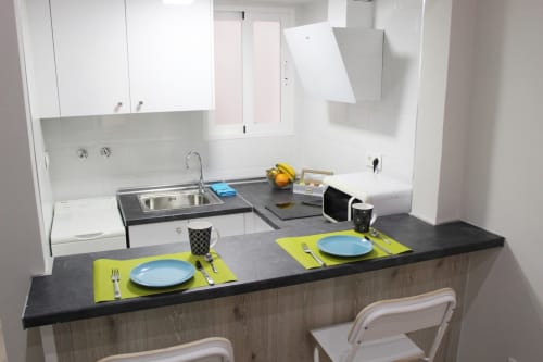 Cocina moderna con barra americana, encimeras oscuras, vajilla colorida y electrodomésticos funcionales.