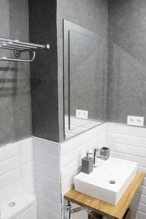 Baño moderno con lavabo sobre madera, azulejos blancos tipo metro, paredes grises y espejo amplio.