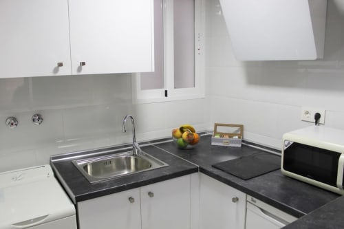 Cocina moderna con encimeras oscuras, muebles blancos, fregadero amplio, microondas y detalles minimalistas.