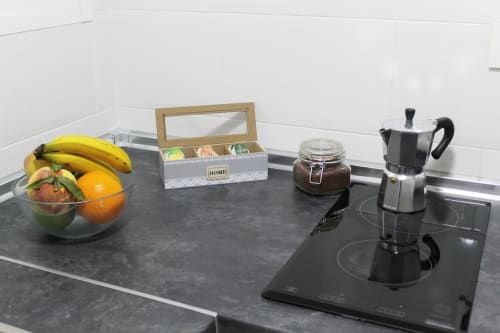 Encimera con vitrocerámica, cafetera italiana, frutero, caja de infusiones y tarro de café, en cocina moderna.