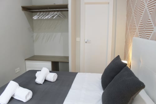 Habitación moderna con cama doble, almohadas grises, papel tapiz geométrico y armario abierto minimalista.