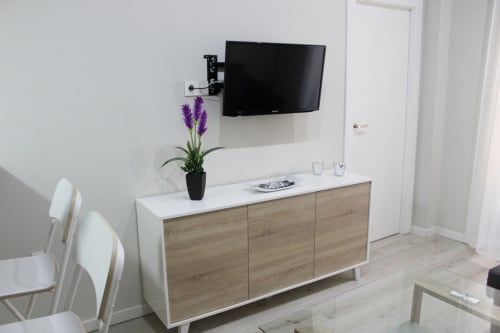 Zona de estar con mueble de madera clara, televisor montado, decoración floral y diseño moderno y minimalista.