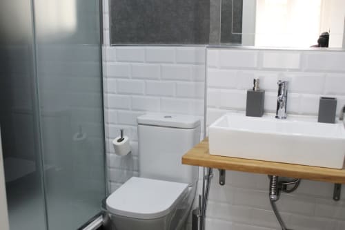 Baño compacto con azulejos blancos tipo metro, lavabo moderno sobre madera y ducha con mampara de cristal.