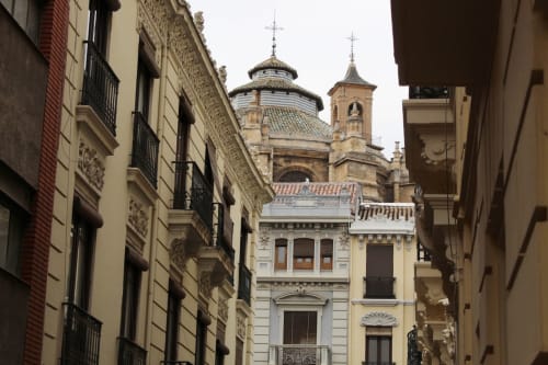 Vista arquitectónica de calle con edificios históricos y cúpula de iglesia, reflejando el encanto clásico urbano.