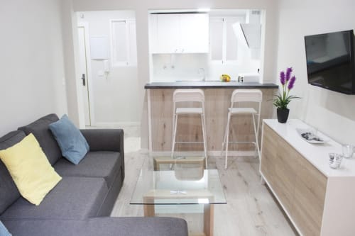 Salón amplio con sofá gris, cojines coloridos, mesa de cristal, barra americana y cocina integrada moderna.