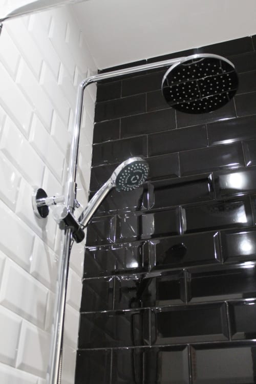 Ducha moderna con azulejos tipo metro en blanco y negro, rociador de techo y grifo ajustable cromado.