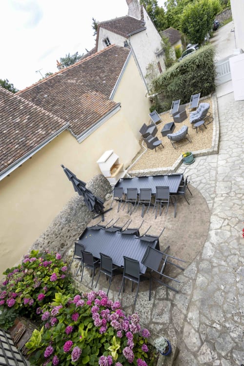 Vue aérienne de la cour du cottage Accolade à Châteaudun avec tables de salle à manger, chaises longues, hortensias roses et bâtisse historique