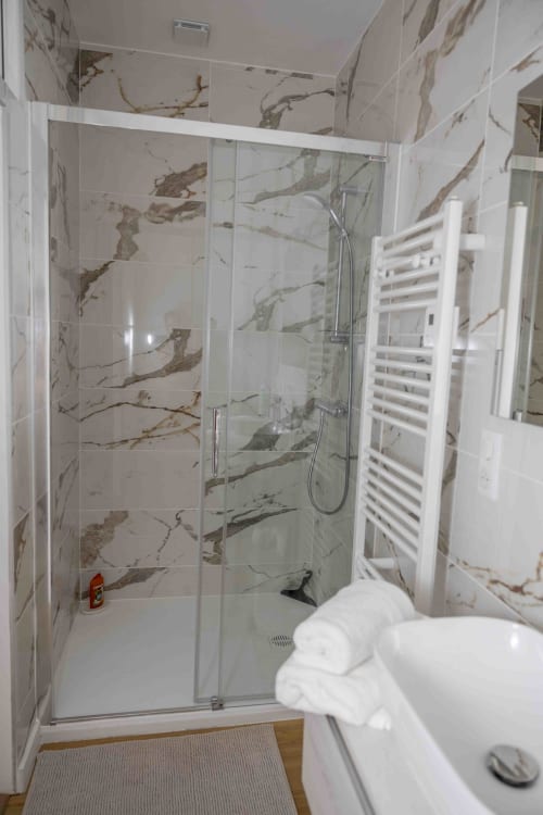 Salle de bains moderne avec paroi de douche en carrelage effet marbre, porte-serviettes blanc et radiateur sèche-serviettes au cottage Accolade