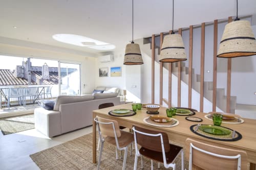 Salle à manger et salon modernes à Finques Garcia Enrich à Palafrugell avec table en bois, luminaires suspendus tressés et vue sur la mer