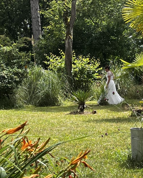 Mujer con vestido blanco paseando por los exuberantes jardines de Domaine de l'Ocrerie, una encantadora casa rural en Pourrain, Francia