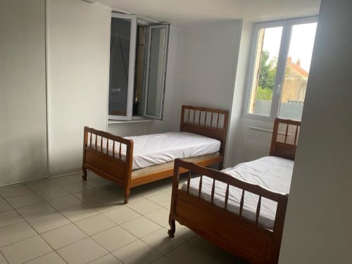 Deux lits jumeaux dans une chambre lumineuse aux Gîtes de Flo, Saint Ennemond, avec sol carrelé et vue sur la cour