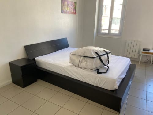 Lit noir moderne avec draps blancs et sac de rangement dans la chambre de l'appartement aux Gîtes de Flo, Saint-Ennemond