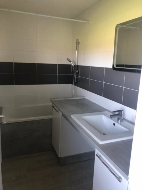 Salle de bain moderne avec lavabo blanc, carrelage foncé et baignoire à la villa Les gîtes de Flo à Saint Ennemond