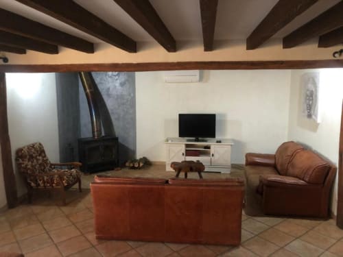 Salon accueillant aux Gîtes de Flo à Saint Ennemond avec poutres apparentes, canapé cuir, cheminée et télévision