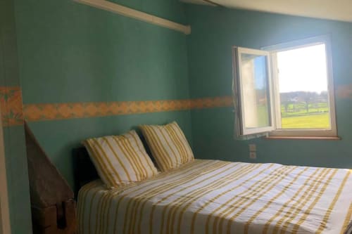 Chambre aux murs bleu canard, literie rayée, vue sur les jardins verdoyants à la villa Les gîtes de Flo à Saint Ennemond