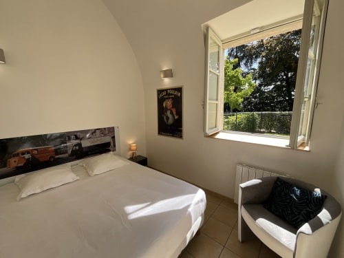 Bright bedroom at Locacharme cottage in Blois with white bed, garden view window, vintage poster, and seating area