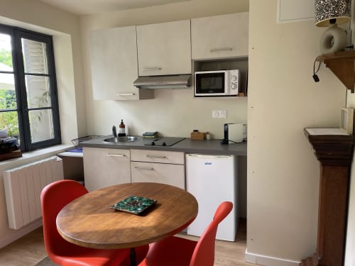 Modern kitchen-dining area at Clairseine cottage with cream cabinets, wood table, red chairs, and garden view window