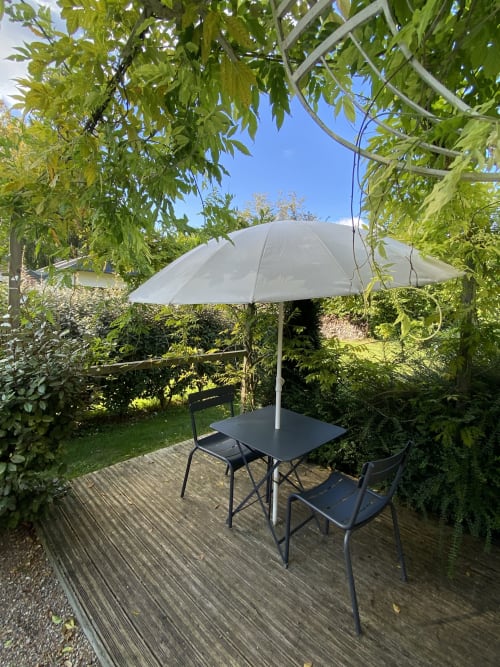 Garden seating area at Clairseine BnB with shaded patio table, umbrella, and lush greenery in Tournedos-sur-Seine